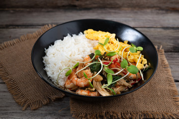 Rice topped with stir-fried shrimp and basil, and fried eggs in white dish.