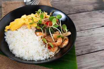 Rice topped with stir-fried shrimp and basil, and fried eggs in white dish.