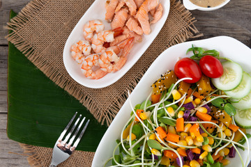 Fresh salad plate with shrimp, salmon, tomato and mixed greens  on wooden background .