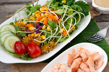 Fresh salad plate with shrimp, salmon, tomato and mixed greens  on wooden background .