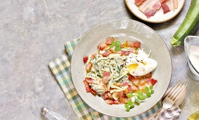 Low-Carb keto carbonara pasta with spaghetti (noodles) of zucchini with cream, fried bacon and poached egg. decorated with pea sprouts. in a beautiful light dish. top view.  copy space