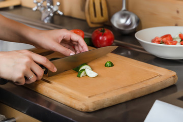  Female hands cut a cucumber on the board