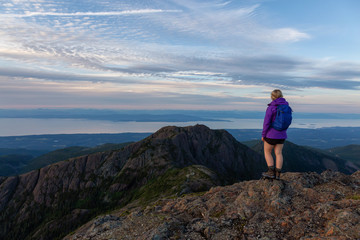 Naklejka na ściany i meble Adventurous girl hiking the beautiful trail in the Canadian Mountain Landscape during a vibrant summer sunset. Taken at Mt Arrowsmith, near Nanaimo, Vancouver Island, BC, Canada.