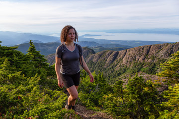 Naklejka premium Adventurous girl hiking the beautiful trail in the Canadian Mountain Landscape during a vibrant summer evening. Taken at Mt Arrowsmith, near Nanaimo, Vancouver Island, BC, Canada.
