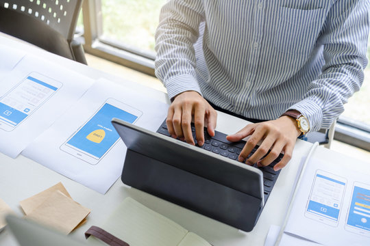 Concentrated male in casual working or typing on smart keyboard tablet for designing , coding, programing mobile application from prototype and wireframe layout. 