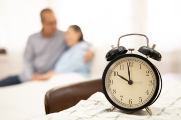 Senior couple at home. clock on the table . Handsome old man and attractive old woman are hugging and enjoying spending time together while sitting on bed.