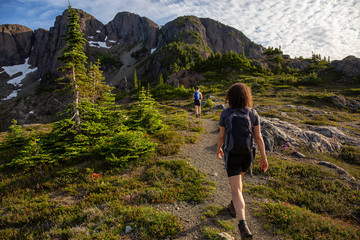 Naklejka na ściany i meble Adventurous girl hiking the beautiful trail in the Canadian Mountain Landscape during a vibrant summer evening. Taken at Mt Arrowsmith, near Nanaimo, Vancouver Island, BC, Canada.