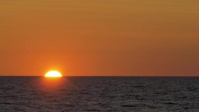 Romantic sunset over the calm Baltic sea, big red Sun sets over the horizon in summer, medium shot from a distance