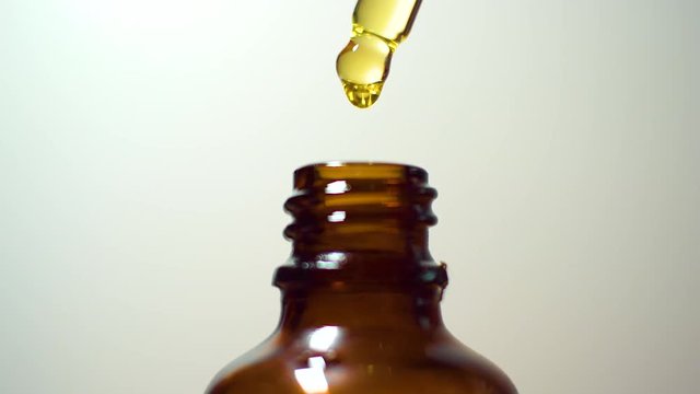 Golden oil in classic rustic brown glass bottle macro close-up isolated with background beads of oil dripping out of droplet dropper