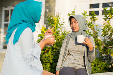 close up happy shot two hijab women drinking tea and coffee in front of the house and smiling