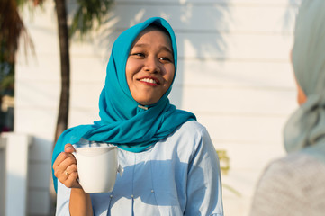 close up happy shot two hijab women drinking tea in front of the house and smiling
