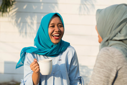 close up happy shot two hijab women drinking tea in front of the house and smiling