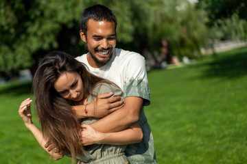 Obraz premium Mixed couple in love is hugging in park during warm summer sunny weather. friend and girlfriend different races love each other. Tolerance, world peace. Lifestyle
