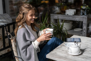 young european girl drinks tea in street cafe during break. Cool weather cover with blanket. girl drinks tea during break from working on tablet, reading e-book. Lifestyle hobby.