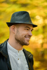 Portrait of a smiling man in a black hat and leather jacket on a yellow autumn background. Autumn...