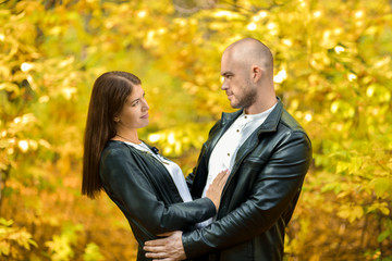 Autumn forest. A dark-haired beautiful girl and a bald brutal man in leather jackets tenderly look...