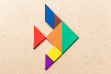 Color tangram puzzle in fish shape on wood background