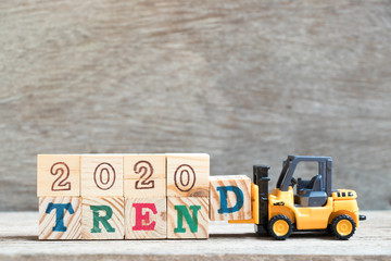 Toy forklift hold letter block d to complete word 2020 trend on wood background