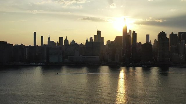 Aerial Drone Camera Pans Left As A Boat Floats By In The Same Direction With A Golden Sunset & New York City In The Background