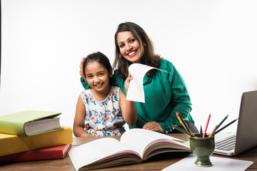 Indian girl studying with mother or teacher at study table with laptop computer, books and having...