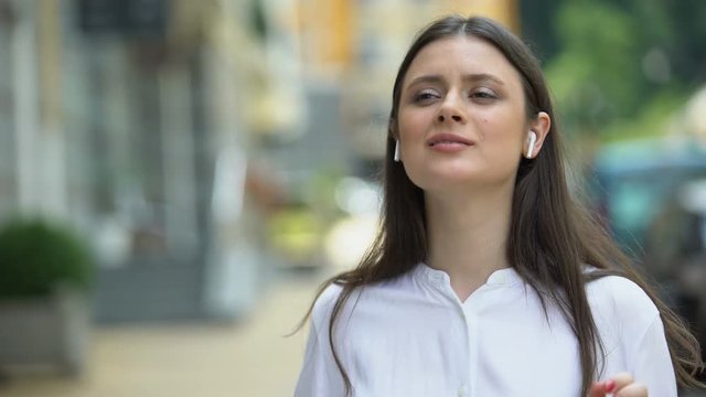 Beautiful woman wearing wireless headphones on city street, enjoying music