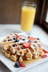 Two pancakes topped with berries, powdered sugar, syrup and orange juice
