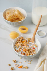 Bowl of granola with dried apricot on white table. Wooden spoon.