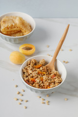 Bowl of granola with dried apricot on white table. Wooden spoon.