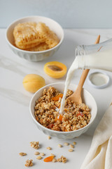 Bowl of granola with dried apricot on white table. Wooden spoon.