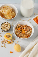 Bowl of granola with dried apricot on white table. Wooden spoon.