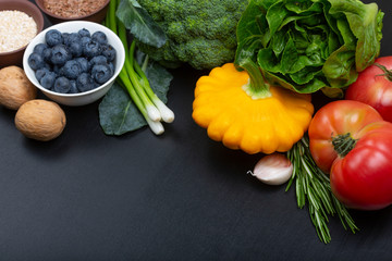 Mix of fresh healthy vegetarian ingredients of vegetables, berries, nuts and cereals on a black wooden background. Copy space.