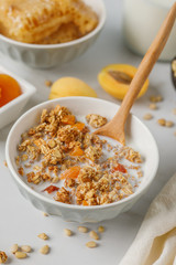 Bowl of granola with dried apricot on white table. Wooden spoon.