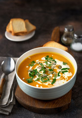 Pumpkin soup with cream and parsley on dark rustic background