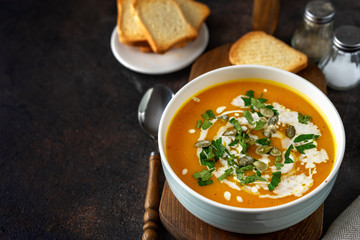 Pumpkin soup with cream and parsley on dark rustic background