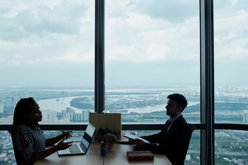 Business people sitting at big table at modern office with panoramic windows and discussing serious issues and plans
