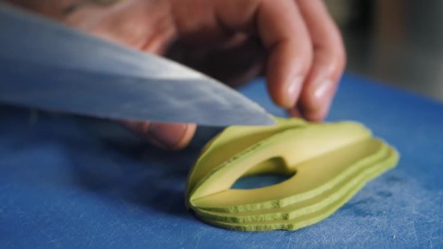 Close up of chef male hands cooking with avocado at table slice knife cut macro
