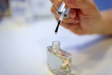 Female hand holding transparent nail Polish, blurred background, close-up. Bottle of clear nail...