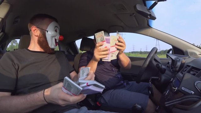 Two men in funny masks with guns in the car rejoice at money after a robbery. Armed robbers used weapons to rob money.