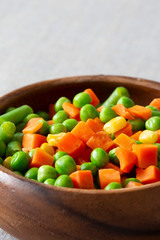 Mixed vegetables, with carrot, beans, peas and sweet corn,  in a wooden bowl.  On a grey textured cotton tablecloth