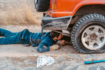 man lies under a 4x4 car on a dirt road