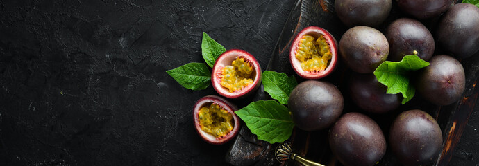 Passion fruits with leaves on a black background. Tropical Fruits. Top view. Free space for text.