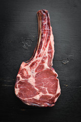 Raw dry steak cowboy on black background. Tomahawk steak. BBQ Top view. Free space for text.