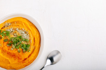 Spicy pumpkin soup served with pumpkin seeds and parsley.  Bowl with autumn squash soup on white table. Top view. Copy space.