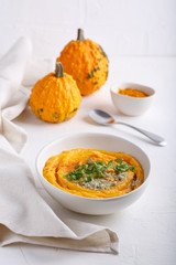 Spicy pumpkin soup served with pumpkin seeds and parsley.  Bowl with autumn squash soup on white table.