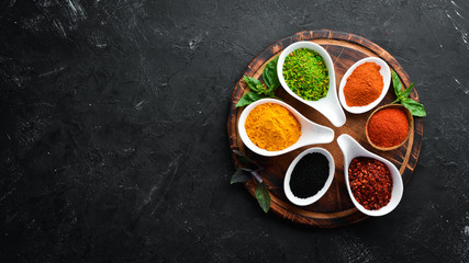 Colorful herbs and spices for cooking. Indian spices. On a black stone background. Top view.