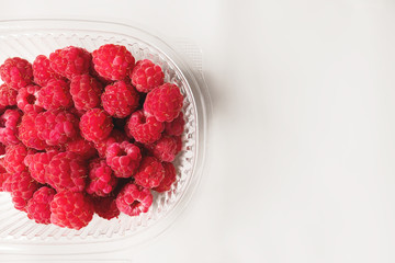 Close-up ripe juicy and delicious raspberry in a plastic transparent dish on a light background. Saturated healthy fresh food