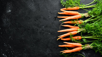 Fresh carrots on a black stone background. Top view. Free space for your text.