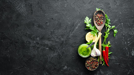 Green parsley sauce, olive oil and spices. Ingredients for chimichurri sauce. On a black background. Top view. free space for your text.