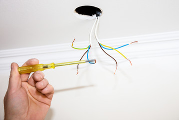 Wires and holes for light bulb in the ceiling. Man holding screwdriver. Electricity maintenance repair works in the flat. Restoration indoors.