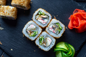 Top view flat lay sushi roll on dark stone plate on dark background with copy space. Roll with avocado and crab. Seafood. Dunk sushi in soy sauce. Concept of Asian cuisine